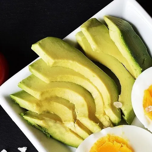 Rodajas de aguacate en abanico junto a medio huevo cocido en un plato blanco rectangular