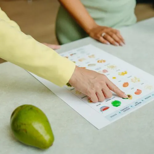 Mujer señala con el dedo una tabla nutricional impresa, con un aguacate verde sobre la mesa