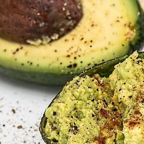 Aguacate cortado en plato blanco, una mitad con hueso y la otra rellena de guacamole sazonado