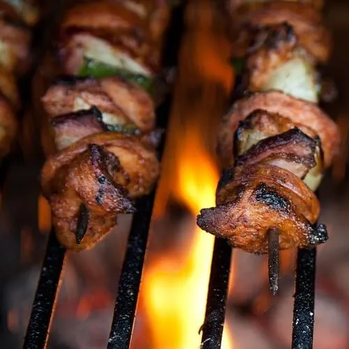 Brochetas de carne asándose sobre llamas vivas en una parrilla a la brasa