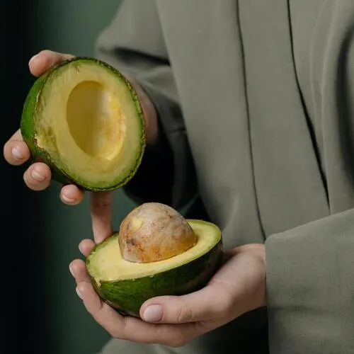 Manos sostienen las dos mitades de un aguacate cortado, una con hueso a la vista