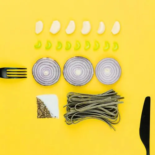 Flat-lay sobre fondo amarillo con rodajas de cebolla morada, ajos, ajíes y cubiertos negros