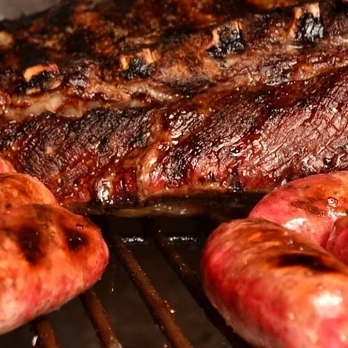 Costillas y chorizos asándose en una parrilla con un glaseado caramelizado