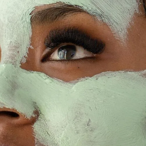 Primer plano del rostro de una mujer con mascarilla verde clara aplicada en la piel
